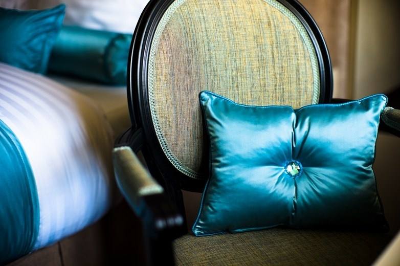 Teal satin cushion with a crystal button on a medallion armchair beside the bed