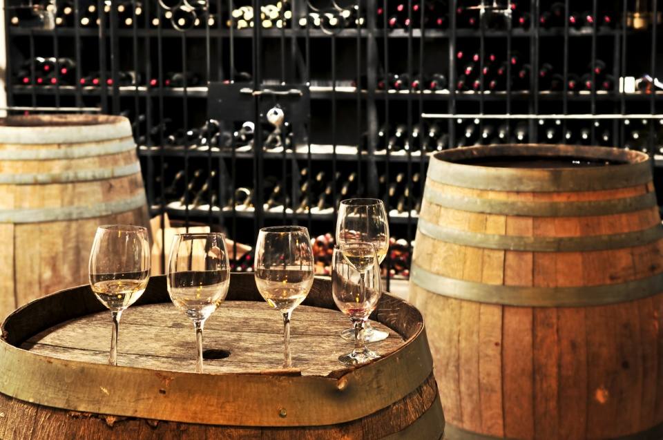Wine glasses on an oak barrel in a wine cellar lined with bottle racks