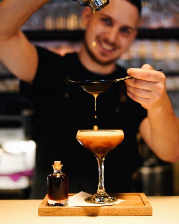 Bartender straining a coffee cocktail into a coupe glass at Jewel Café Bar