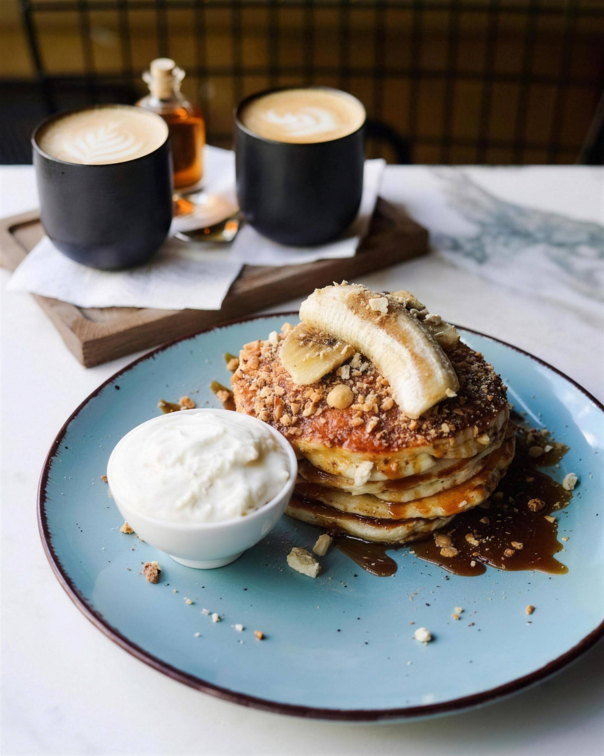 Pancakes with banana, caramel and crumble, a pot of cream and two lattes